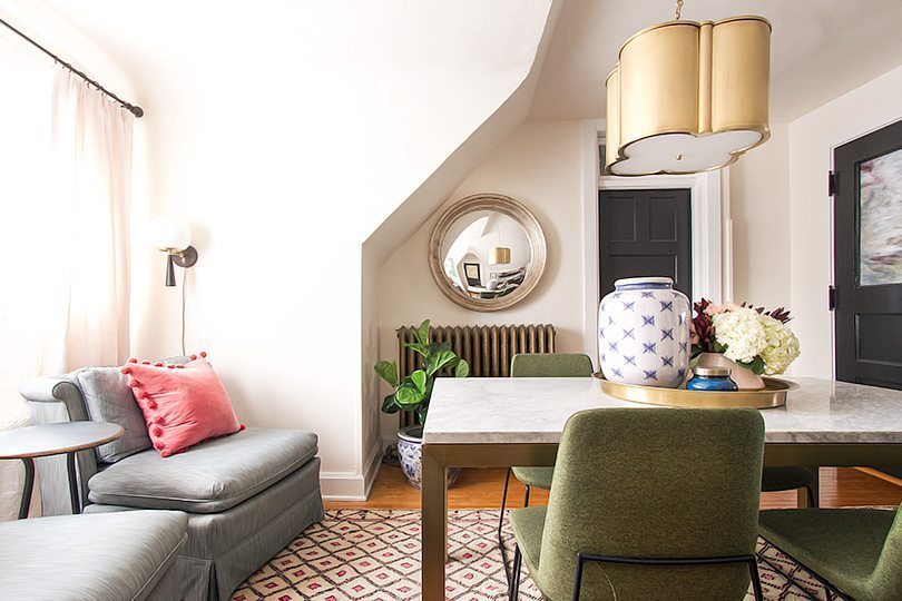 a wide shot of Nicole Balch's office. on the left is the gray sofa with pink cushion. In the middle is the table with a brass pendant lamp hanging from the ceiling. 