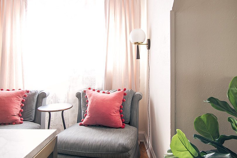 gray vintage slipper chairs with a salmon colored pillow. on the right is a large leafed plant