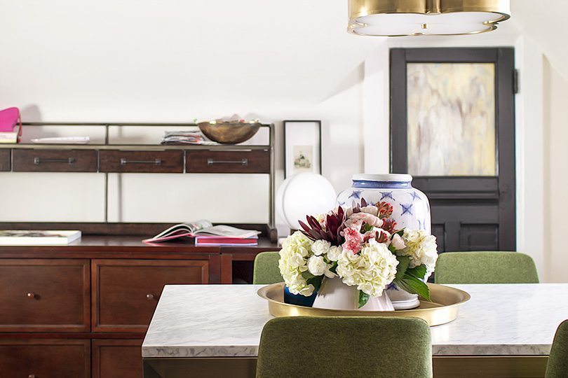 a shot of the table in the middle of the office with a flower arrangement in the center. Behind the table you can see a closed dark door and to the left, a brown shelving unit