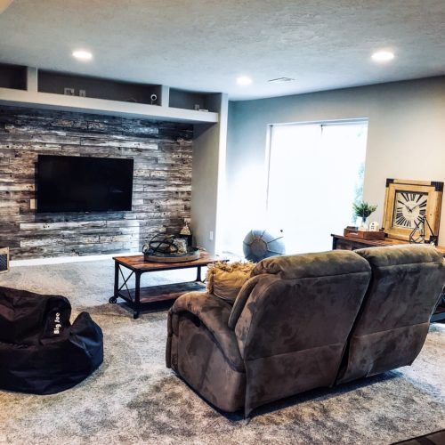 Rustic Wood Panels Wallpaper, wood wallpaper behind a tv screen in a living room with two recliner chairs and a rustic wood coffee table.