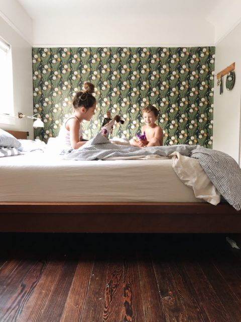 Dandelions Wallpaper on a wall beside a bed with two kids playing in the bed. Dark wood floors