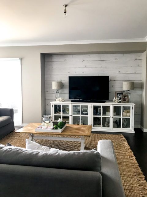 Whitewashed Timber wallpaper behind a television with a gray sofa in the foreground. there is a twill area rug on the floor