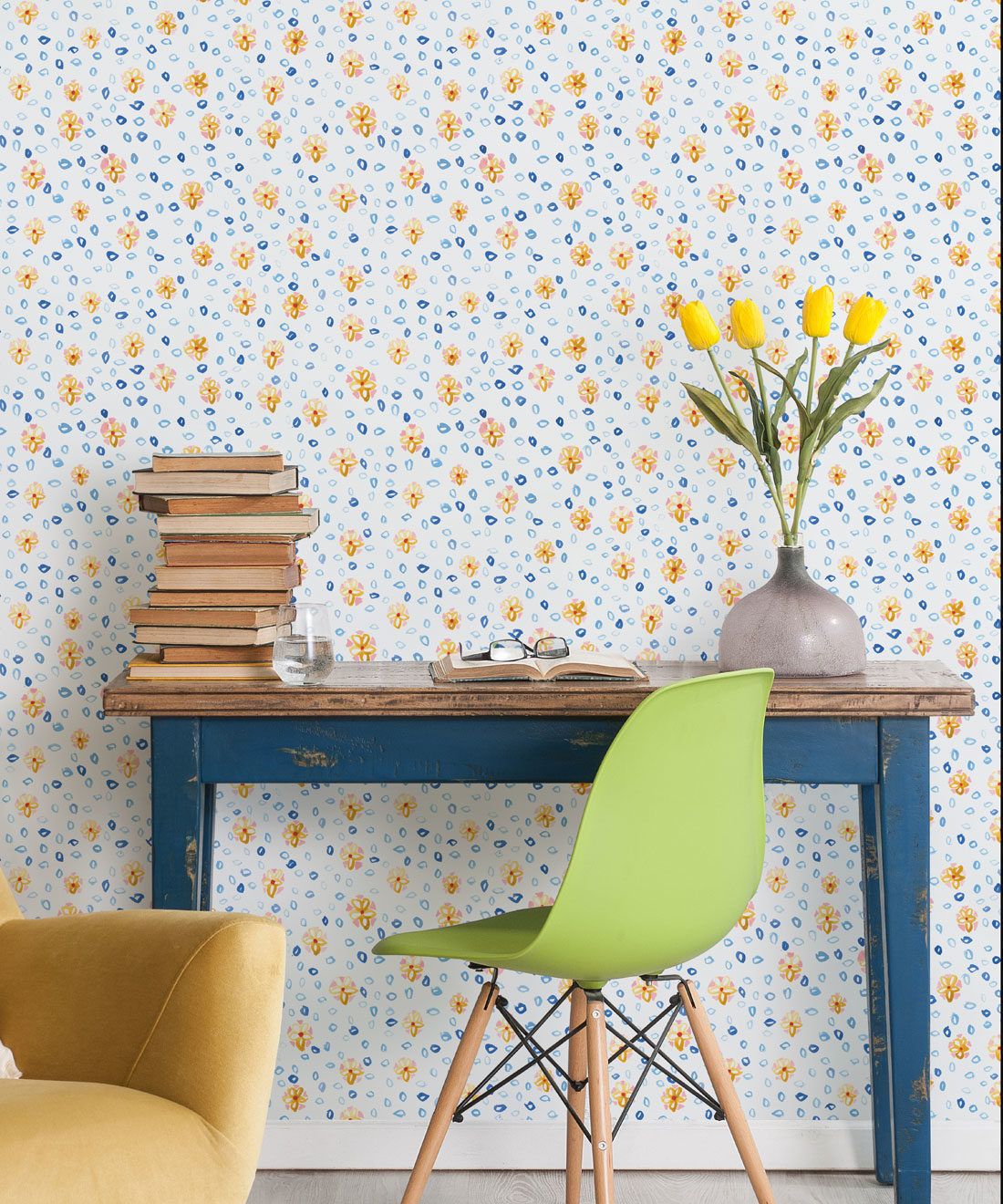 Al Hadiqa Wallpaper • Dainty Floral Design • Desk with books stacked on the left and a lime green chair in front with yellow tulips in a vase on the right side of the desk. • Milton & King USA