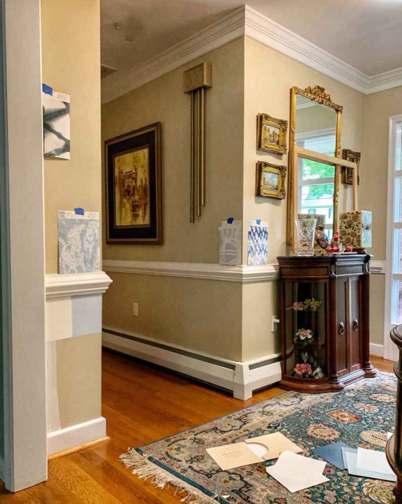 A photo of an entry way with light wood floor boards. There are wallpaper samples stuck to the wall with tape.