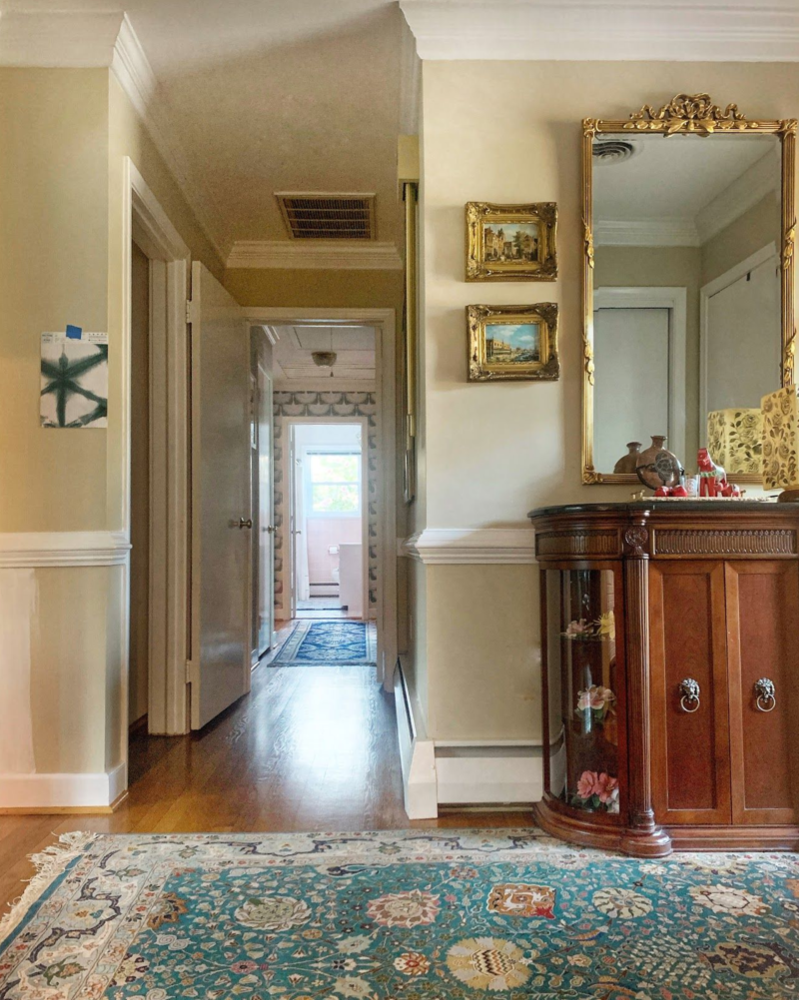 Picture of a hallway with a turquoise area rug. The floor is light wood and the walls are painted beige with a white chair rail.