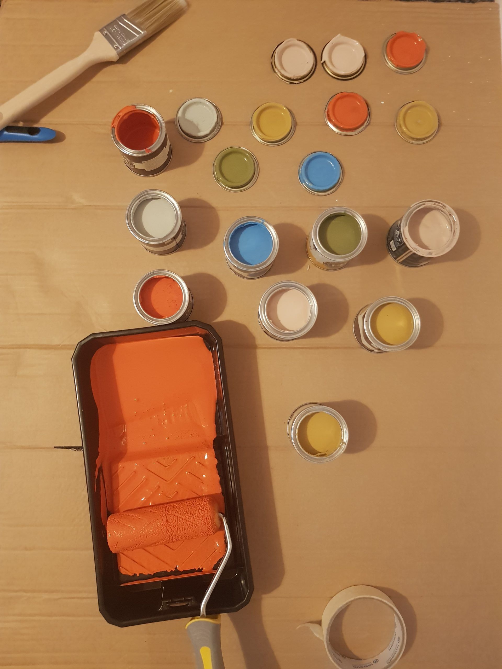 A paint tray with orange paint and several other cans of paint with various colors